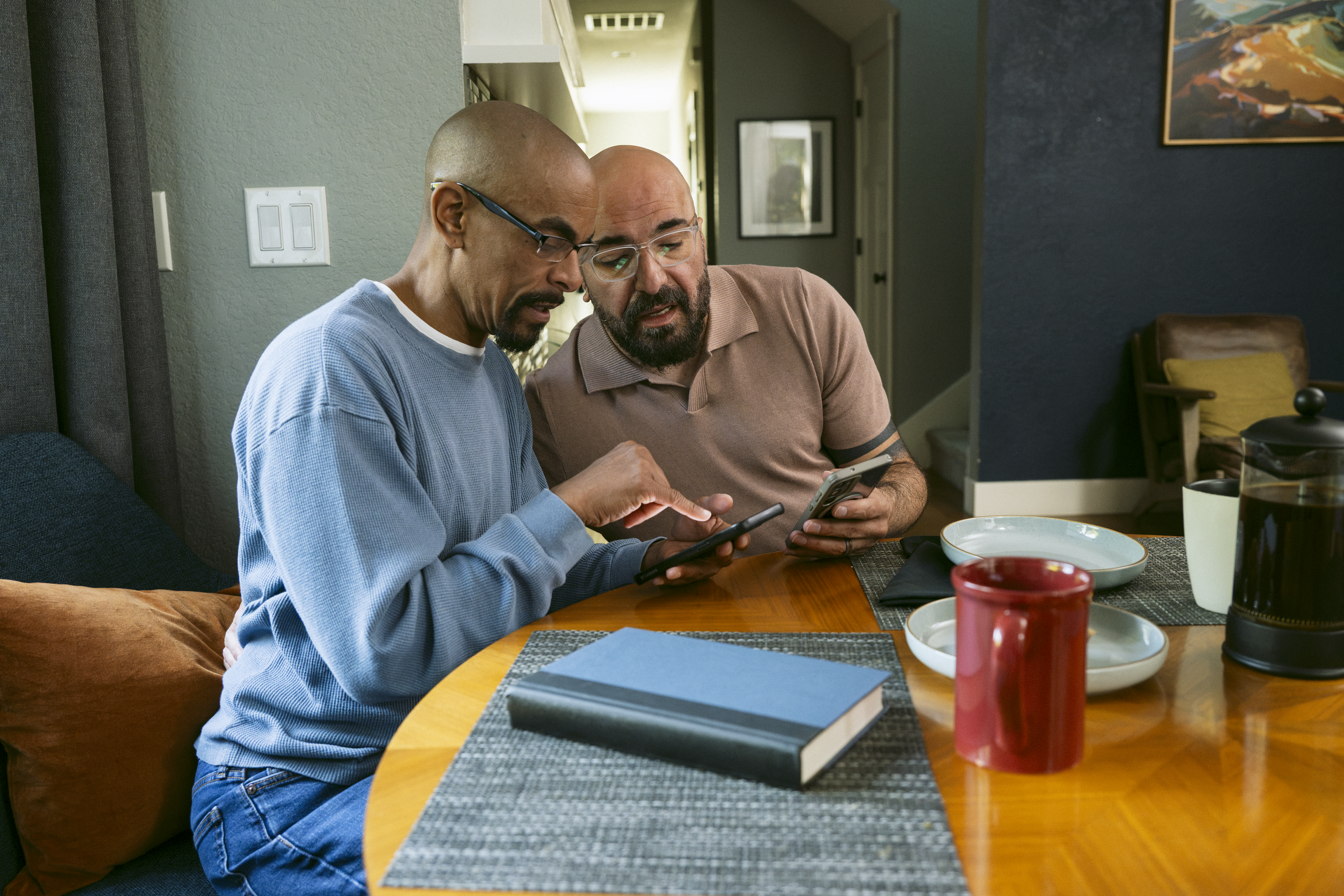 Two men looking at phone at kitchen table.